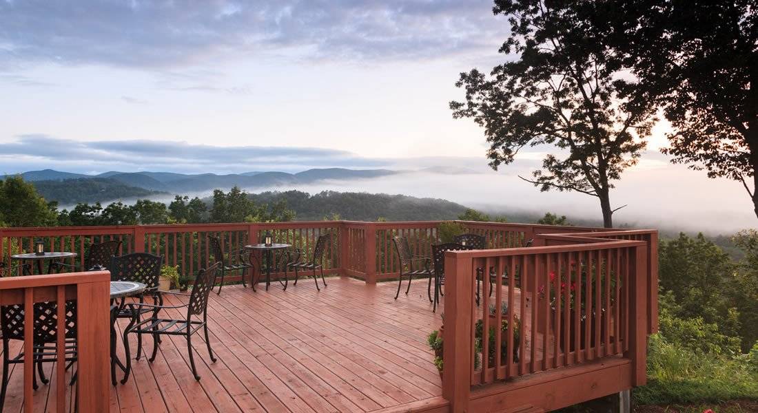 The deck off of the inn with table and chairs and you can see for ever mountains and clouds