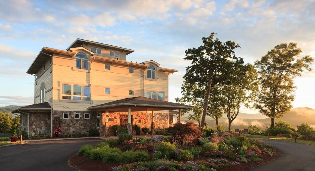 Wide angle of the front of the inn at dusk with the sun setting light on the front, also garden in the circle of the driveway