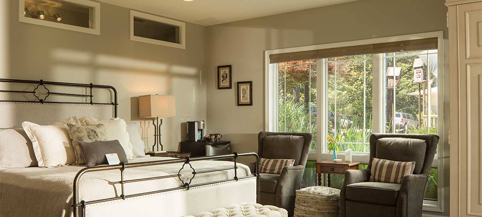 A cast metal bedframe with stuffed chairs underneath large open windows.