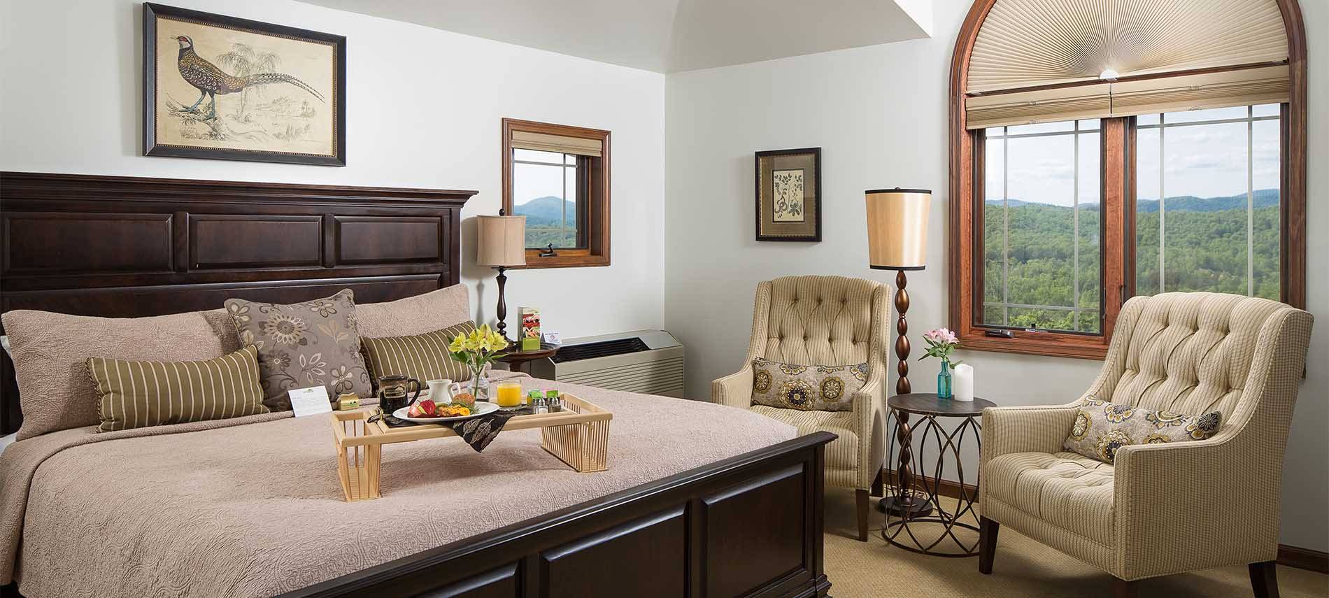 Curved architecture and window frames softly contrast the crips lines of picture frames on walls and the high backed wooden bed frame, with beige morris chairs underneath window.