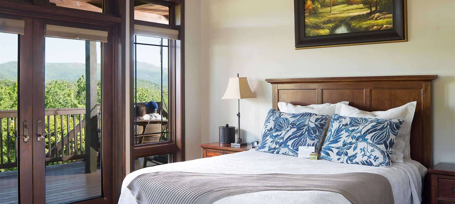 A tall backed wooden bed with blue throws accentuates this bedroom with it's floor to ceiling windows and exterior entry.