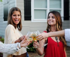 Two women and others toast a glass of mead outdoors.