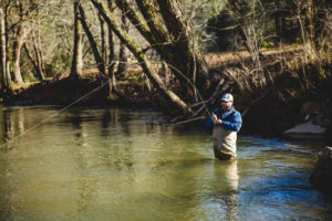 An angler wades in a river waiting for a fish to bite.