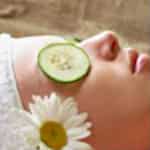 Woman lying down with cucumber slices on her eyes and a daisy in her wrap on her head