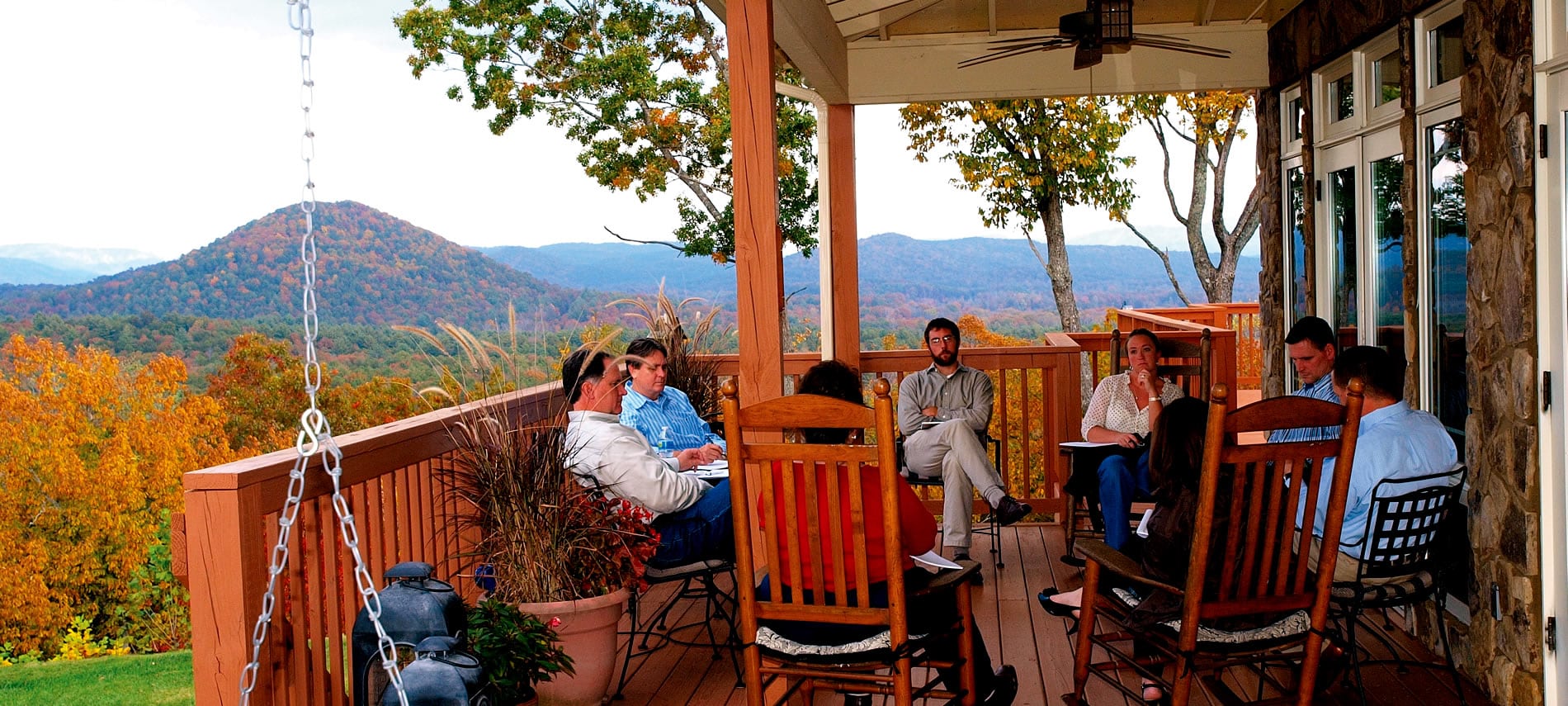 A group of 8 people sitting in chairs on the deck in a circle for a meeting