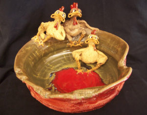 A ceramic bowl with a red bottom and tan top decorated with 3 whimsical ducks