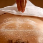 a woman laying on her stomach with a towel covering her lower area with salt being spread over her back