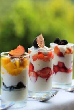 3 glasses with parfait in them with Red Strawberrys and yellow peaches, blueberries