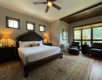 Wood platform bed with leather Headboard lined in brown wood. One tan high back chair and an view of the mountains out the window.