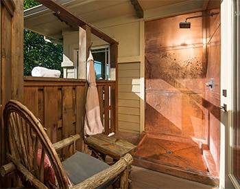 An Exterior located copper shower with old timey shower head and rustic wooden chair. 