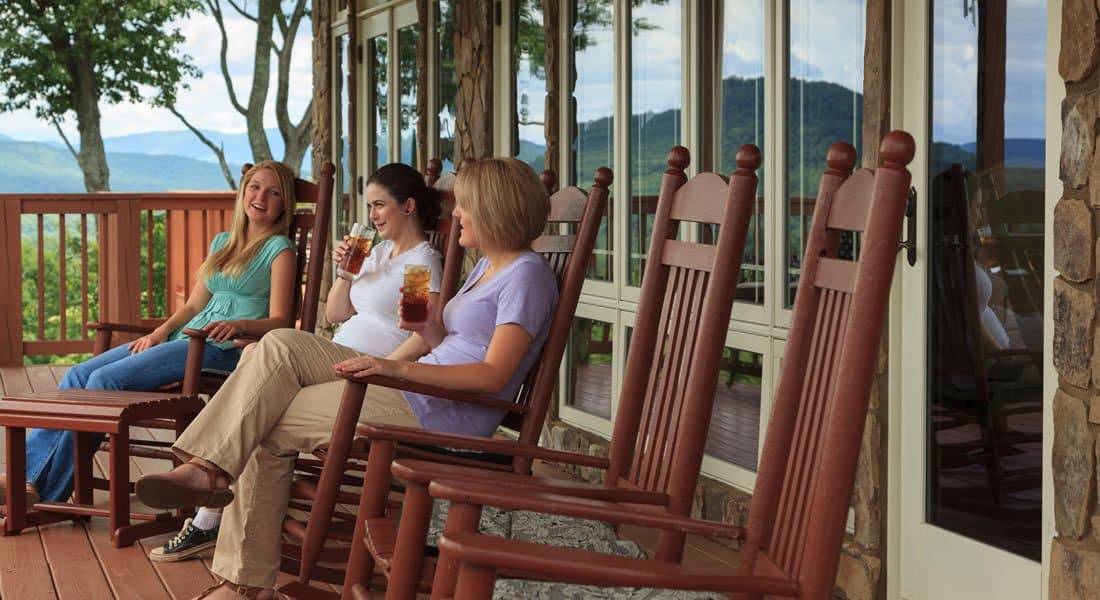 Three women sitting on the porch in brown rocking chairs