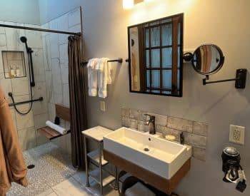 Square grey stone Shower with the stone continuing on the bathroom floor. Floating white sink outlined in wood