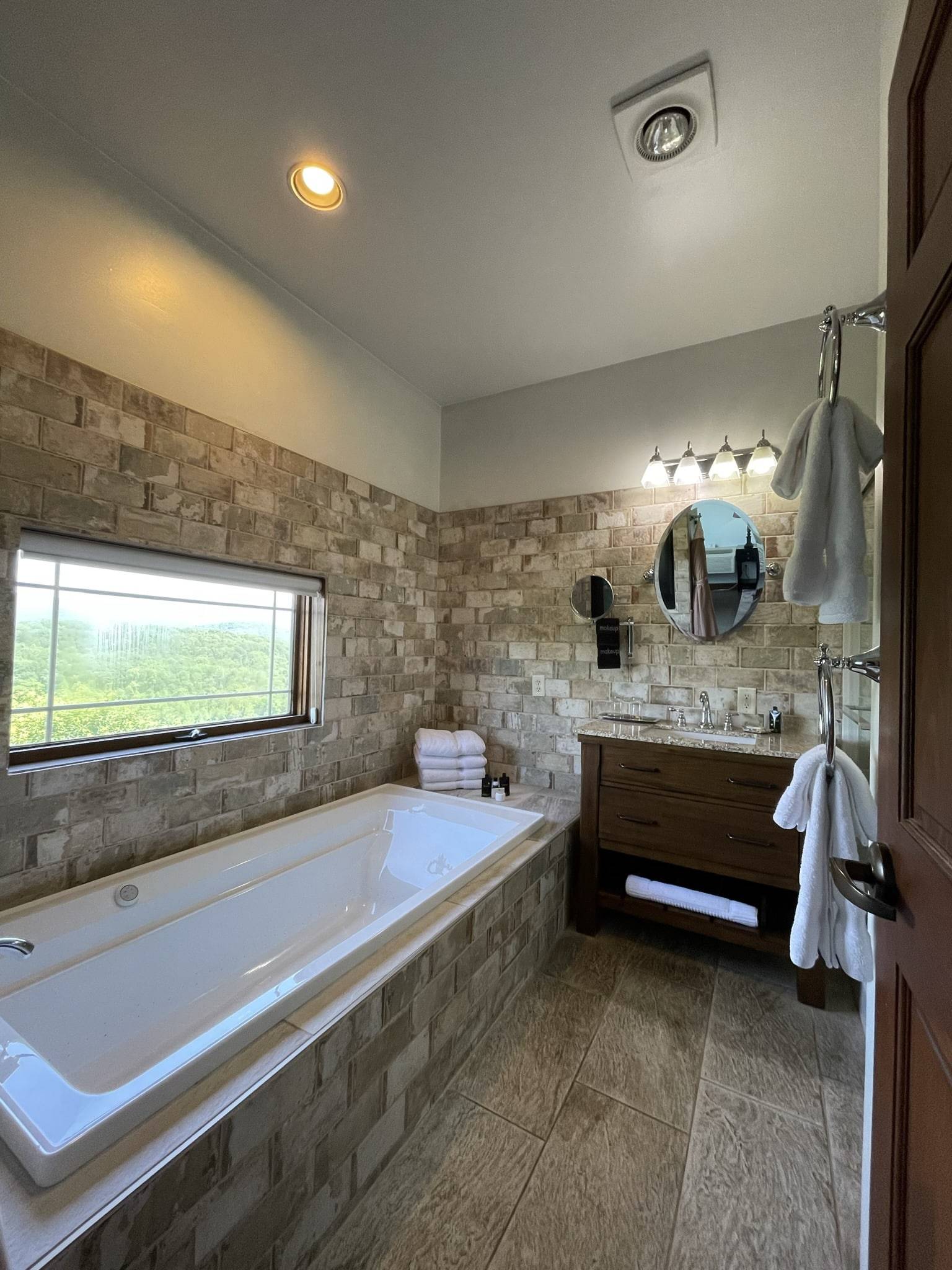 Bathroom sink with a wood cabinet, stone brick walls with a glass enclosed shower. Fluffy white towels sitting next to the soaking tub