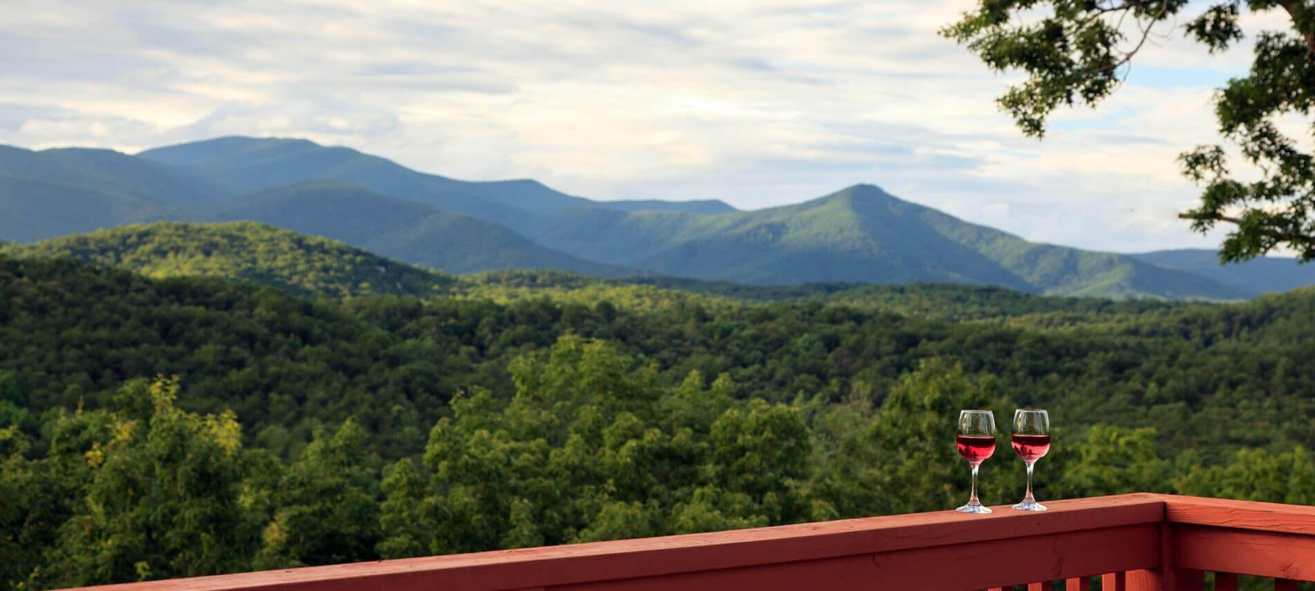 Gorgeous view of the mountians with Two glasses of red wine on the edge railing of the deck