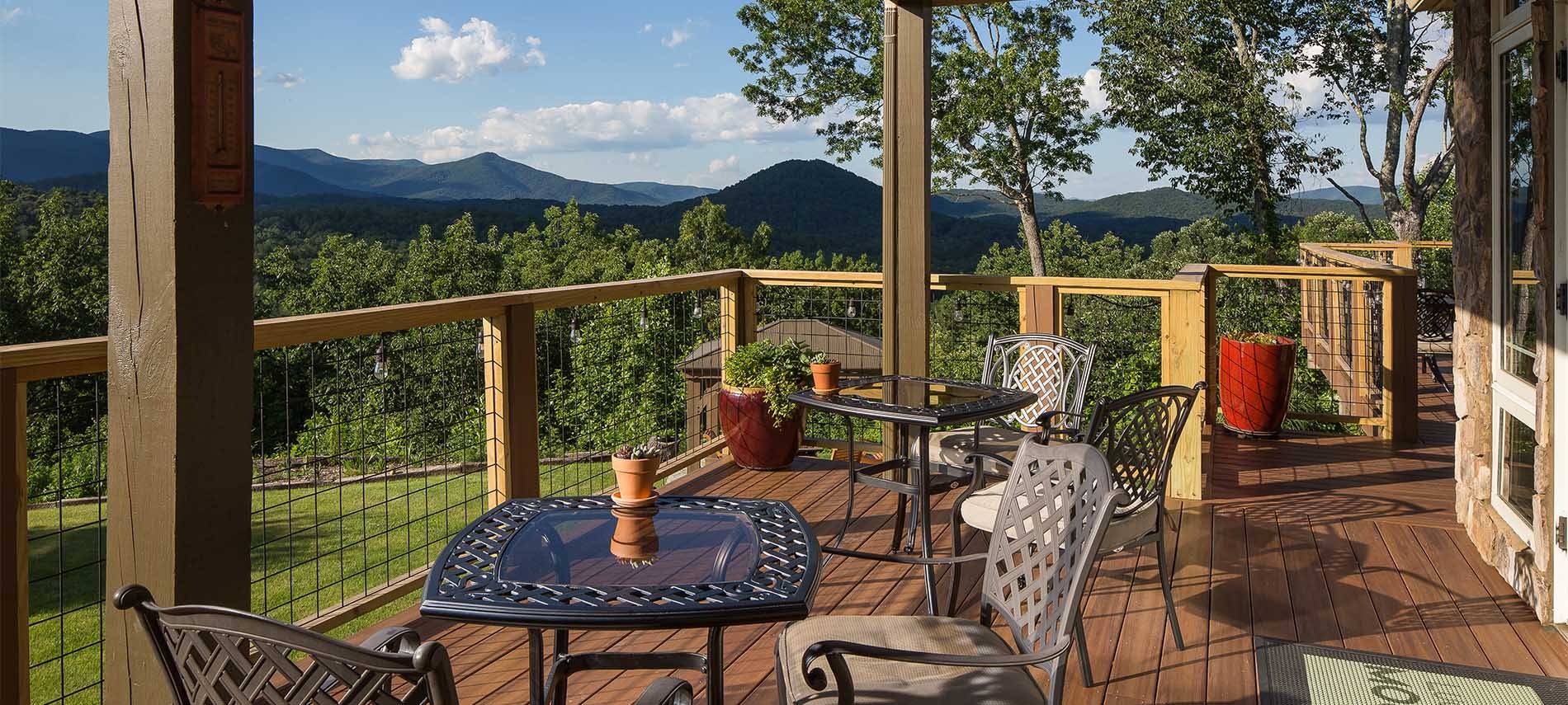 Outdoor patio with reflective dining tables, overlooking a scenic mountain view with sparse clouds dotting the sky.