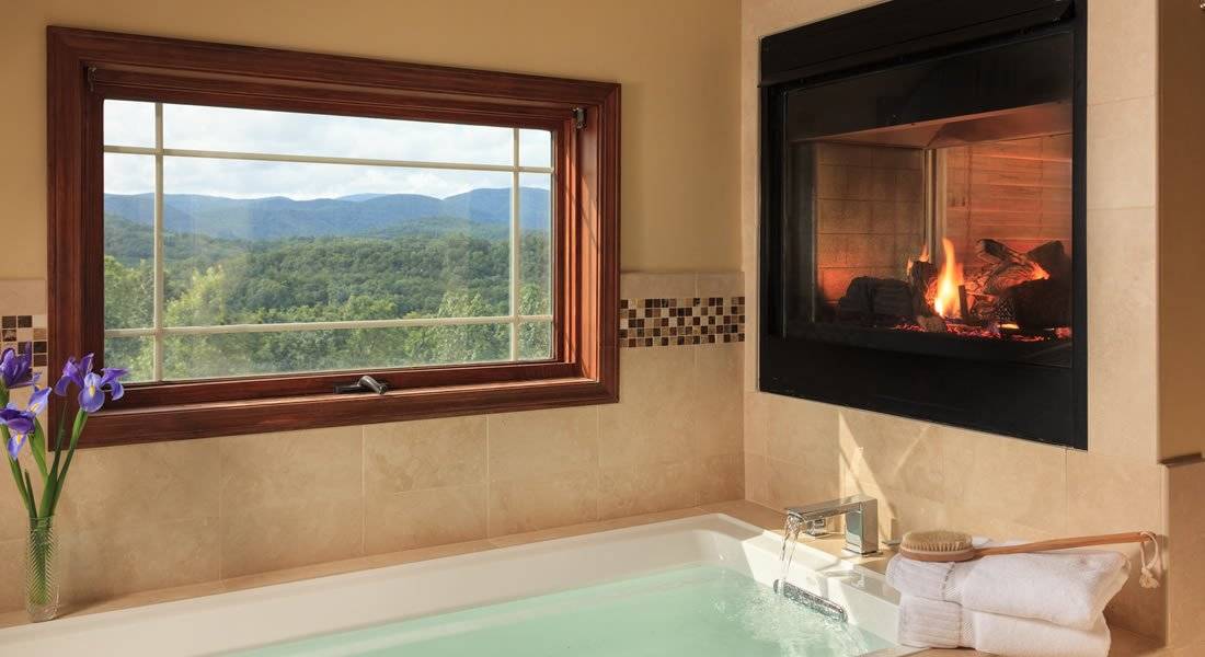 soaking tub filled with water and fluffy towels. Gas see thru fireplace and a window to look out at the view of mountains