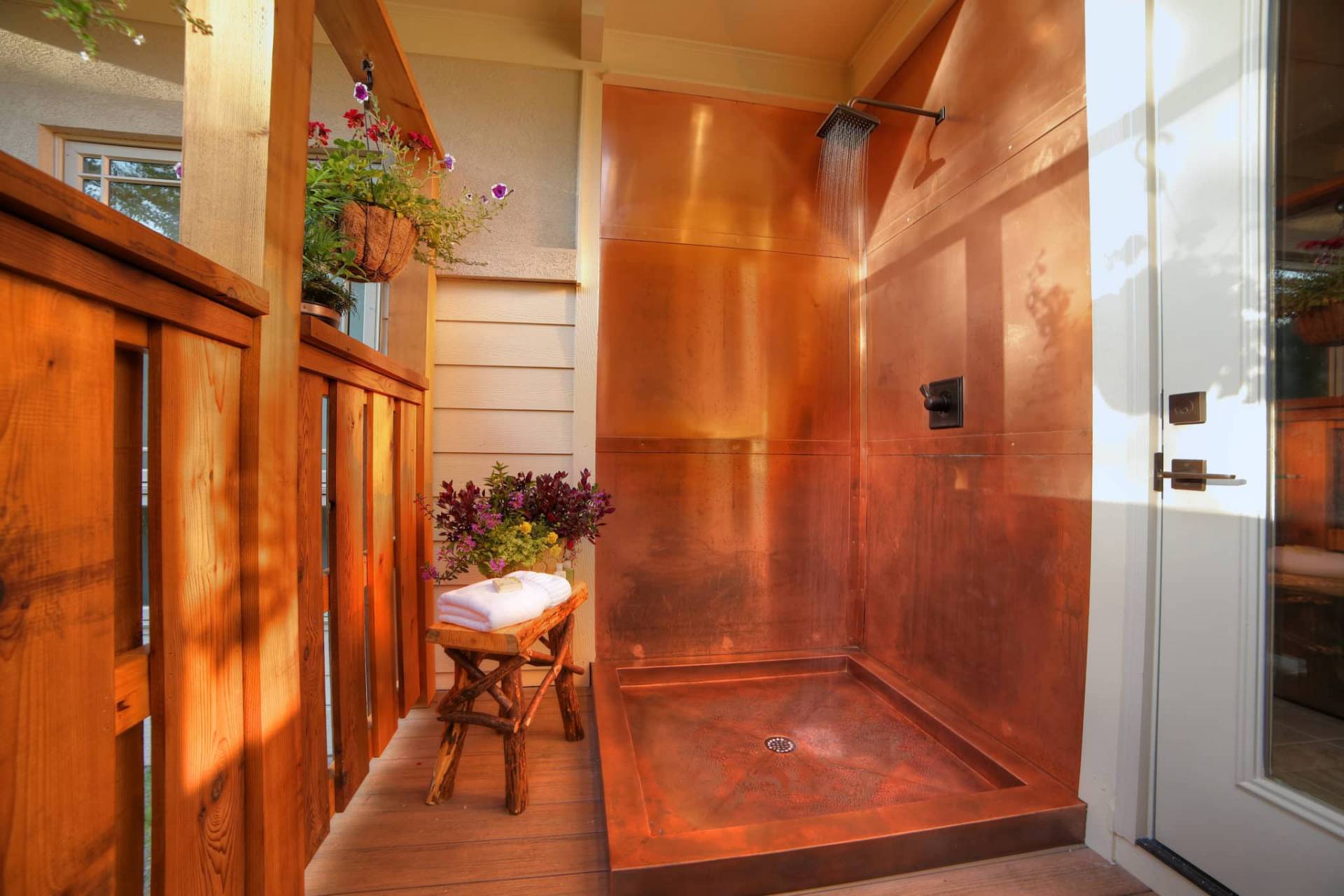 An Exterior located copper shower with old timey shower head and rustic wooden chair. 
